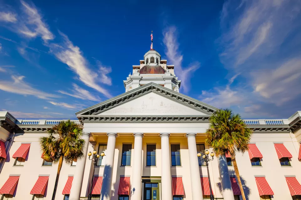 White and peach Florida state capitol building with palm trees in front in Tallahassee, Florida.